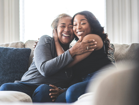 Older woman and younger woman hugging and smiling while sitting on a couch.