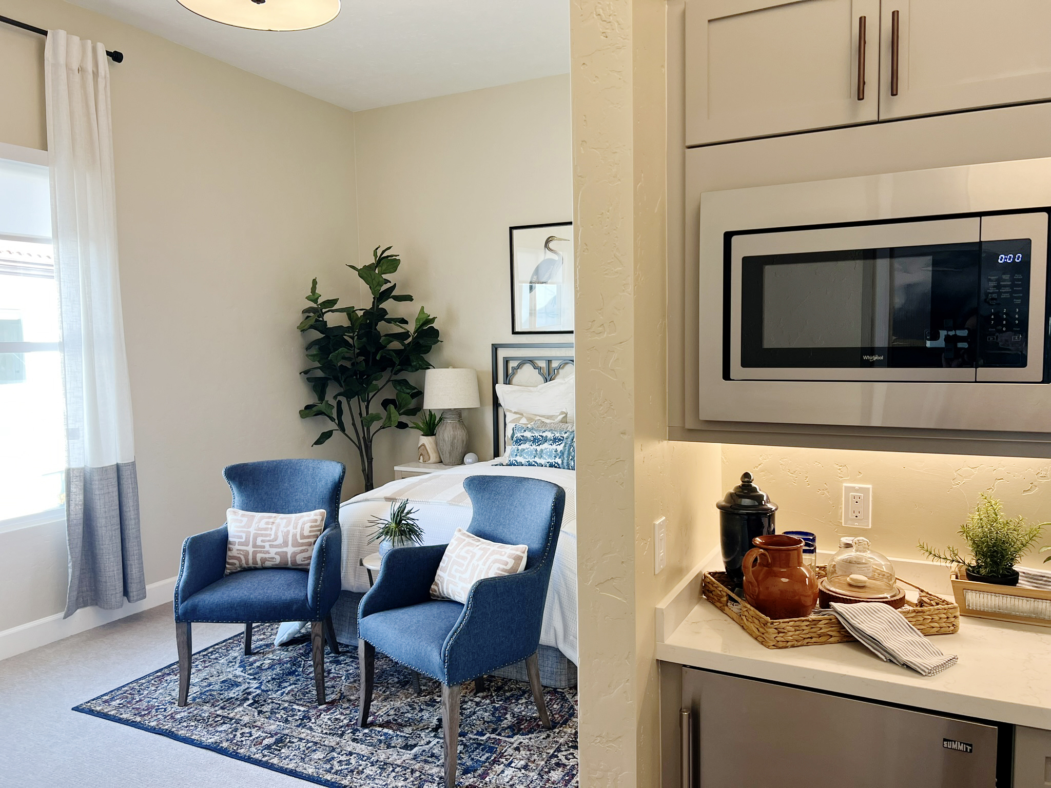 Studio apartment with a window, bed, two charis, and kitchenette.
