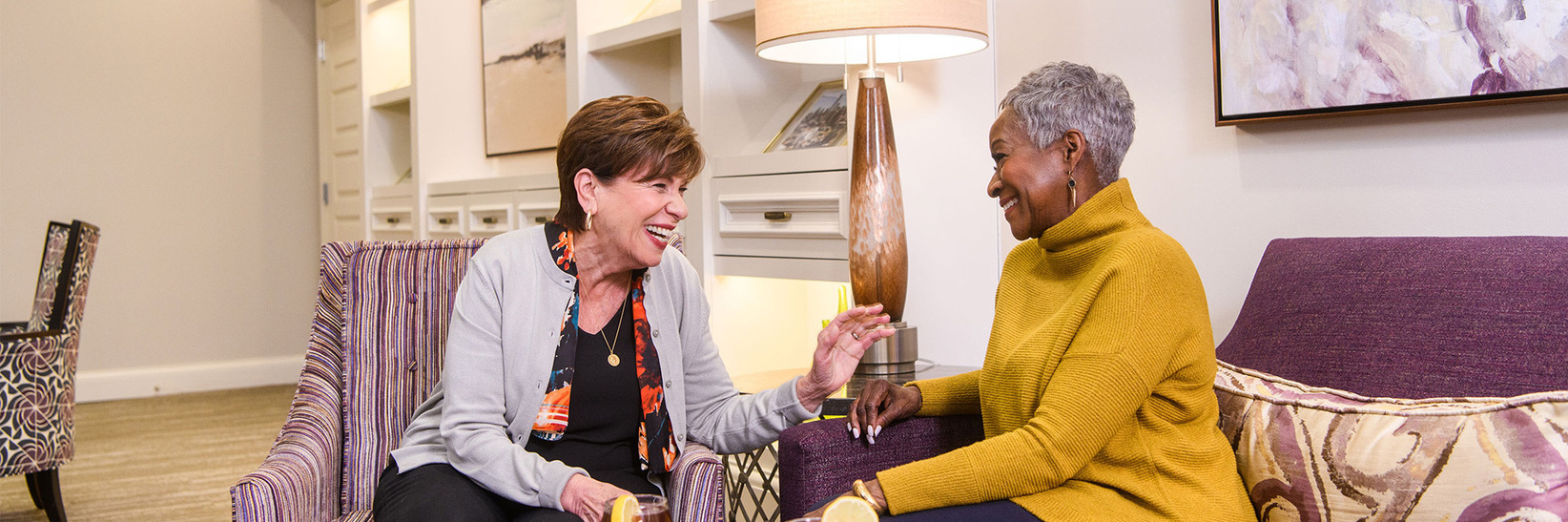 Two friends sitting with drinks at The Preston of the Park Cities Assisted Living Community. Two friends sitting with drinks at The Preston of the Park Cities Assisted Living Community.