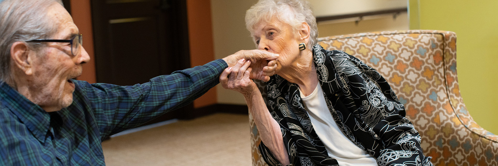 A resident sitting in a chair kissing their partner's hand. A resident sitting in a chair kissing their partner's hand.