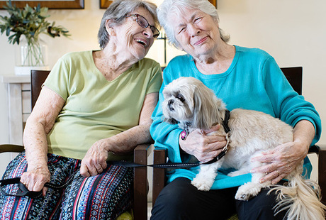 Two residents of The Watermark at Cherry Hills, a senior living community in Albuquerque, sitting down holding a dog.