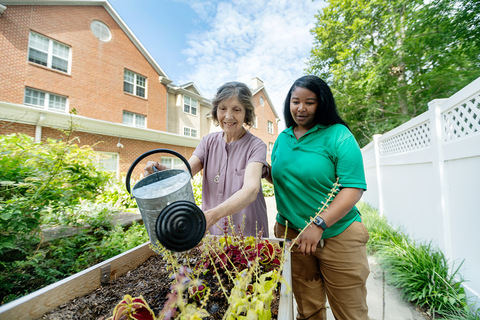 A resident watering plants with a caregiver.