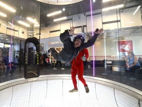 Indoor sky diving. Resident flying while instructor is standing next to them.