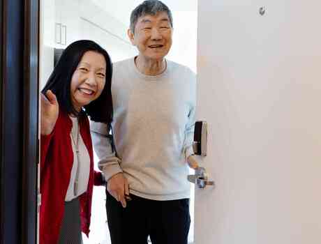 Two residents smile from the doorway of a bright apartment, offering a warm sense of welcome and home.