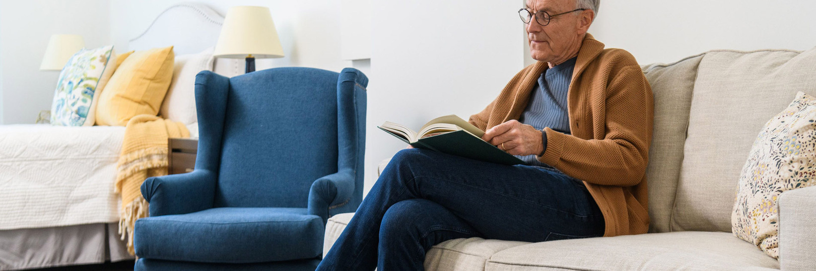 A resident is sitting on a sofa reading a book. A resident is sitting on a sofa reading a book.