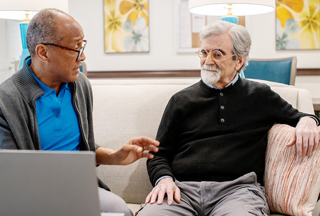 Two people talking with a computer on the table.