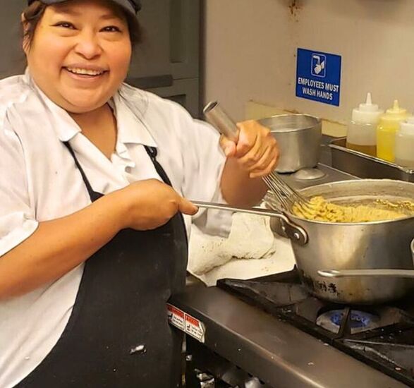 Reyna, a chef, is in the kitchen smiling and cooking.