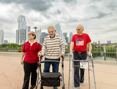 Two residents walking with a caregiver with a cityscape behind them.