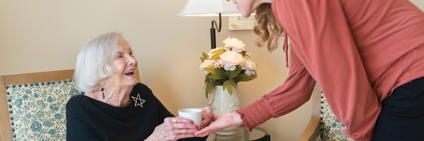 A person handing an assisted living resident coffee at The Watermark at the Peark in Portland.