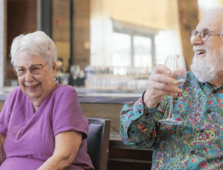 Two residents holding wine glasses at a dinner table and laughing.