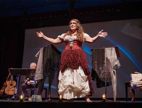 Performer on the stage. She is dressed in period costume. Stage interior of Theatre during performance at night.