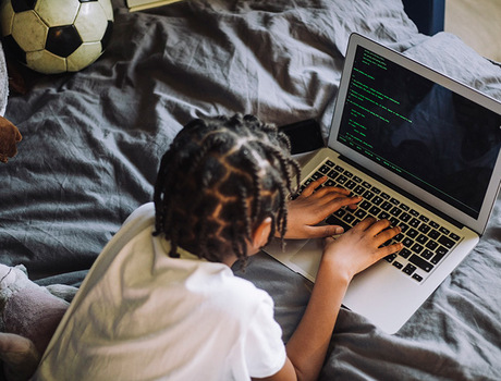 A child laying on the bed with a computer.
