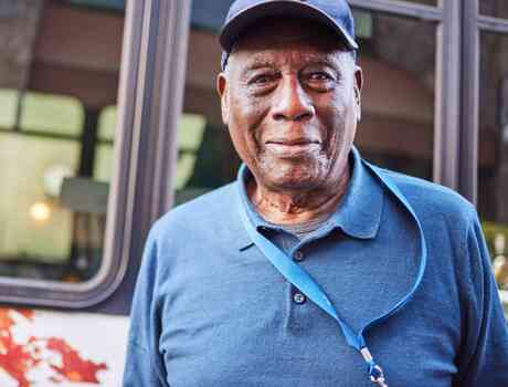A resident stands smiling near the community bus, capturing a sense of connection, independence, and everyday ease.