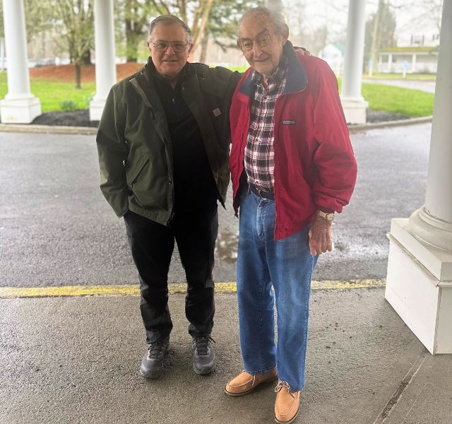 Two people standing together. One has their arm around the other.