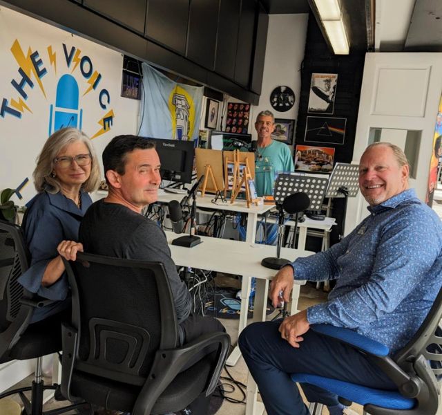 Four people sitting in room recording a podcast.