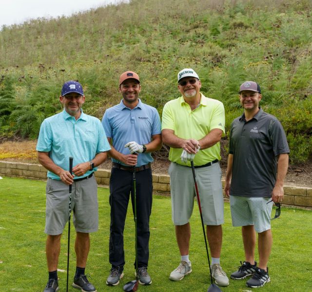 Four golfers smiling and holding golf clubs.