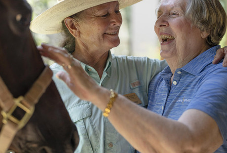 A resident and an associate in the stables petting a brown horse at The Hacienda at the River, assisted living community in Tucson, AZ.