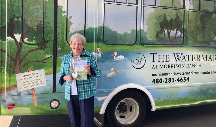 A resident is standing next to a Watermark bus holding her book.