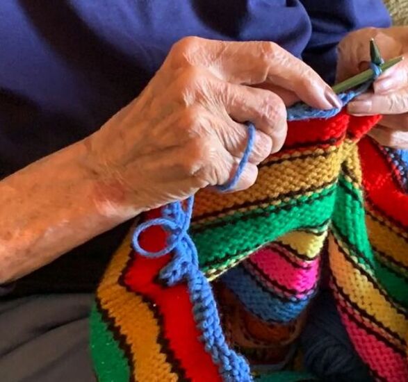 Close up of hands knitting a brightly colored striped sweater.