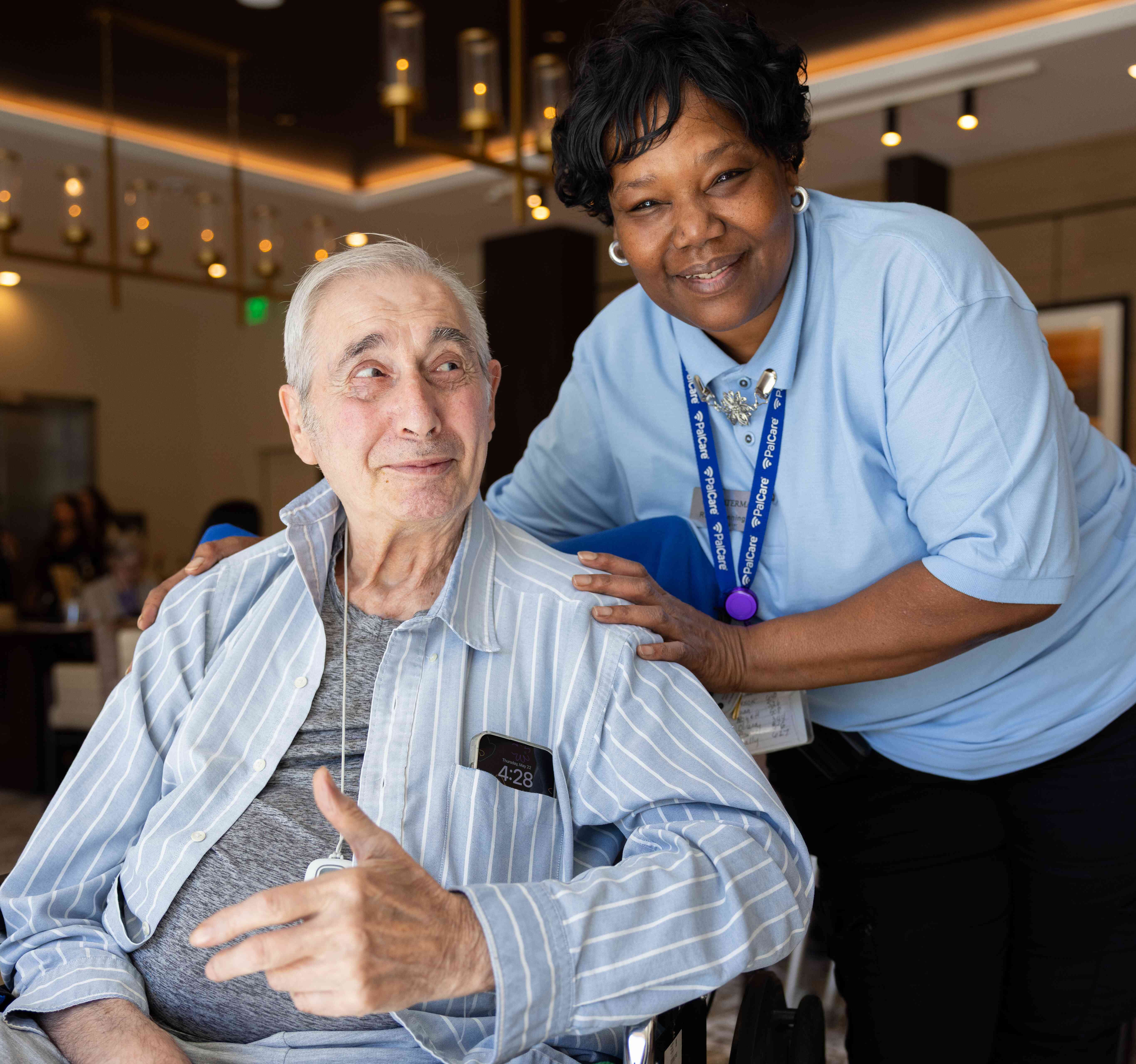Resident in wheelchair wearing PalCare with associate smiling next to him.
