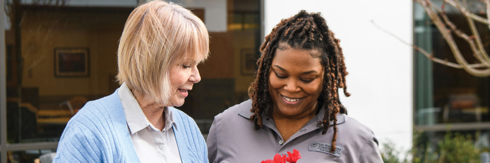 A resident and a caregiver are outside looking at flowers. A resident and a caregiver are outside looking at flowers.