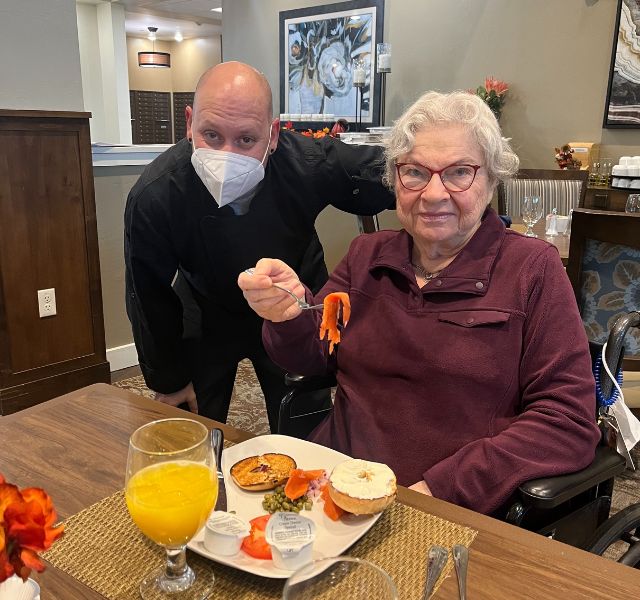 Associate wearing a mask and a resident eating a homemade meal.