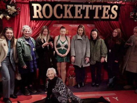 Resident doing the splits in front of the Rockettes step and repeat wall.