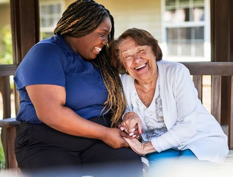 A resident and associate sit close together outdoors, laughing and holding hands during a warm, joyful moment.