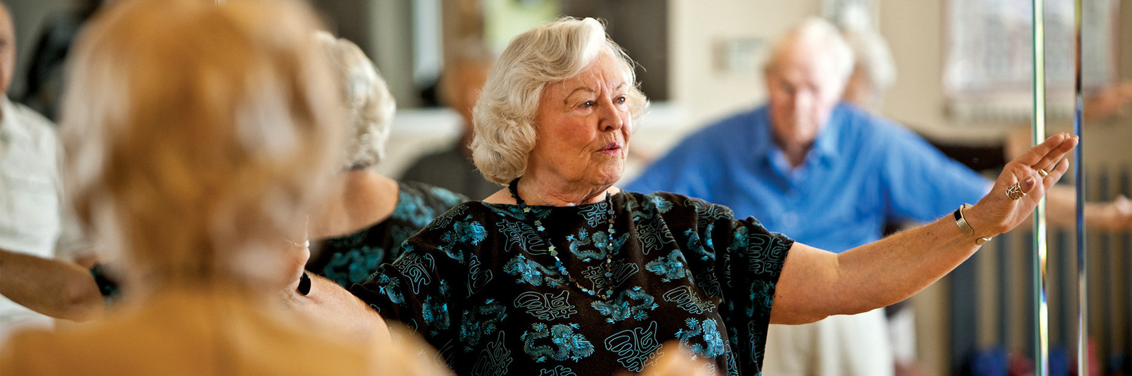 A resident is standing with their arms out on each side during a tai chi class. A resident is standing with their arms out on each side during a tai chi class.