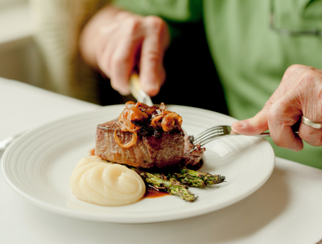 Close-up of steak and potatoes with someone in green shirt cutting into the steak.