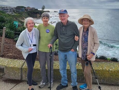 Four residents in tennis shoes and walking poles, standing on lookout over the ocean.