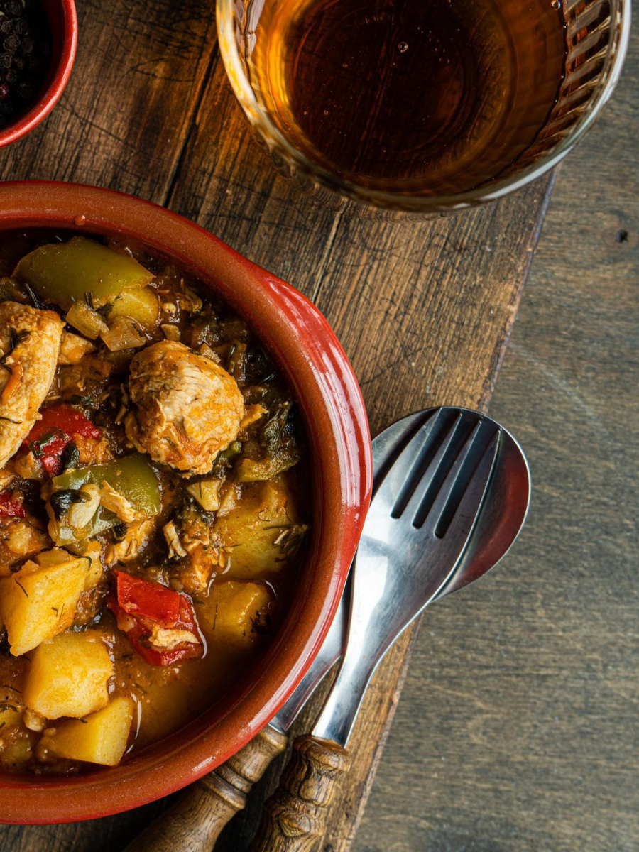 Chicken Curry in orange bowl. Spoon and fork rest on wooden table next to it.