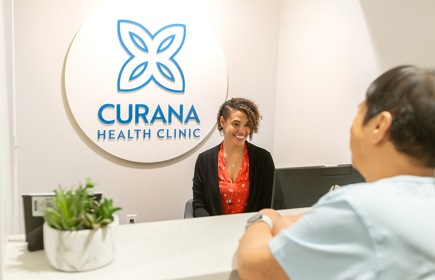 A clinic front desk with a receptionist and patient.