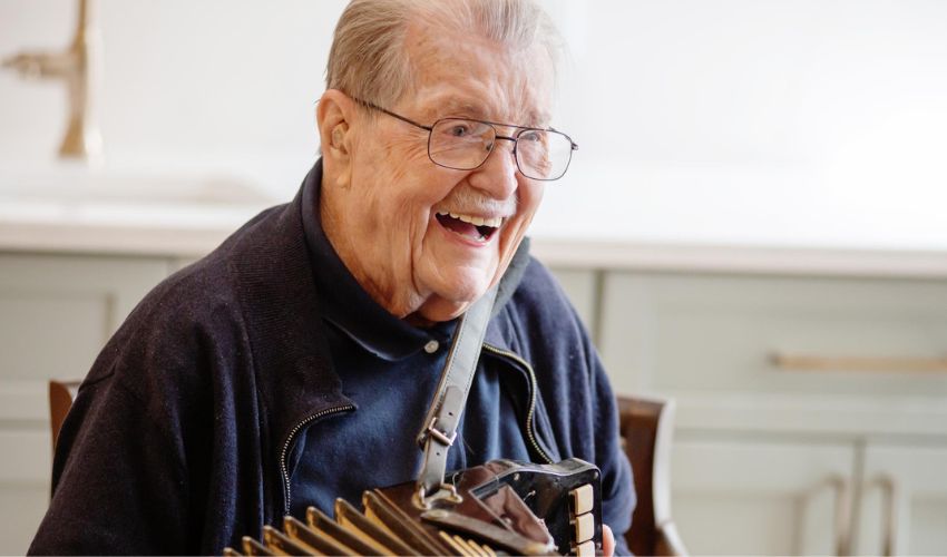A resident is smiling and holding his accordion.