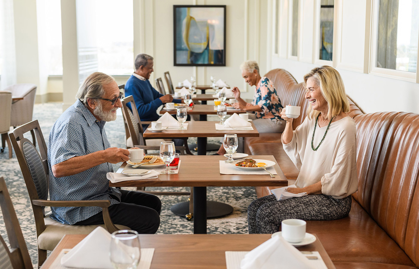 Residents are chatting and sitting at tables in a restaurant enjoying their meals.
