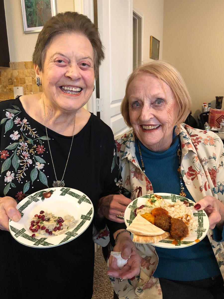 Suad, a resident, with another resident smiling and holding plates of food Suad cooked.