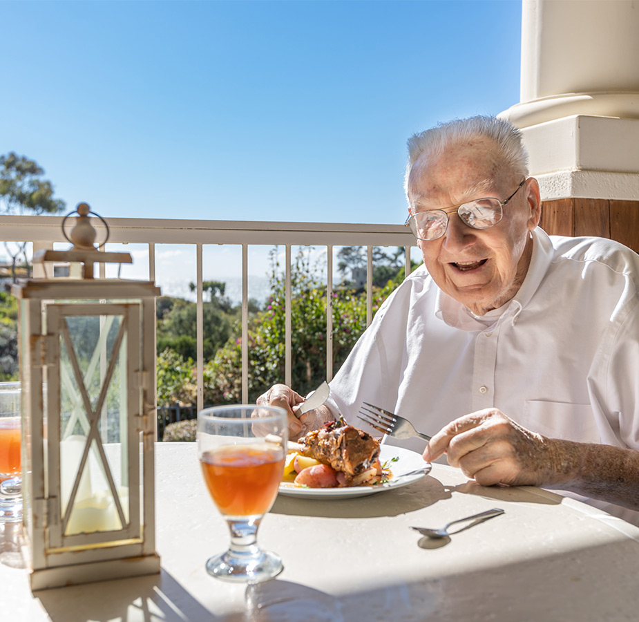 A smiling resident is enjoying a meal at a dining table on the patio.