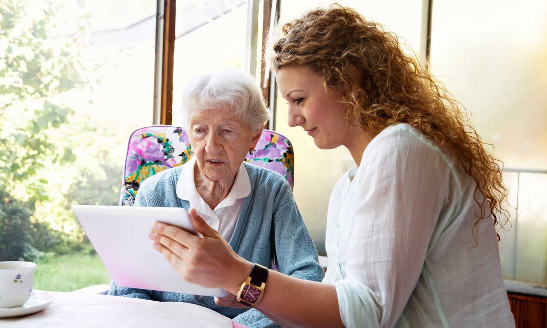 A caregiver is helping a resident use a tablet.