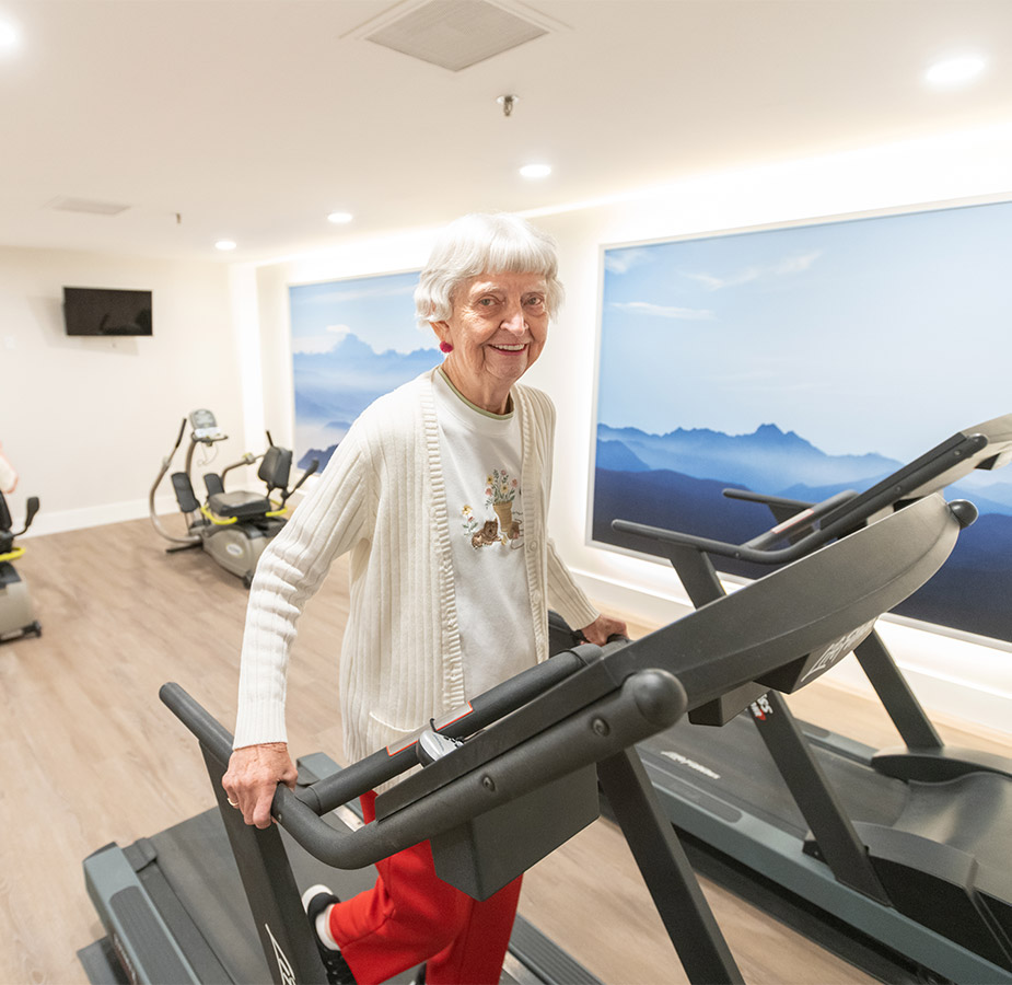 Elderly woman walking on a treadmill in the fitness centre A resident walking on a treadmill in the fitness center.