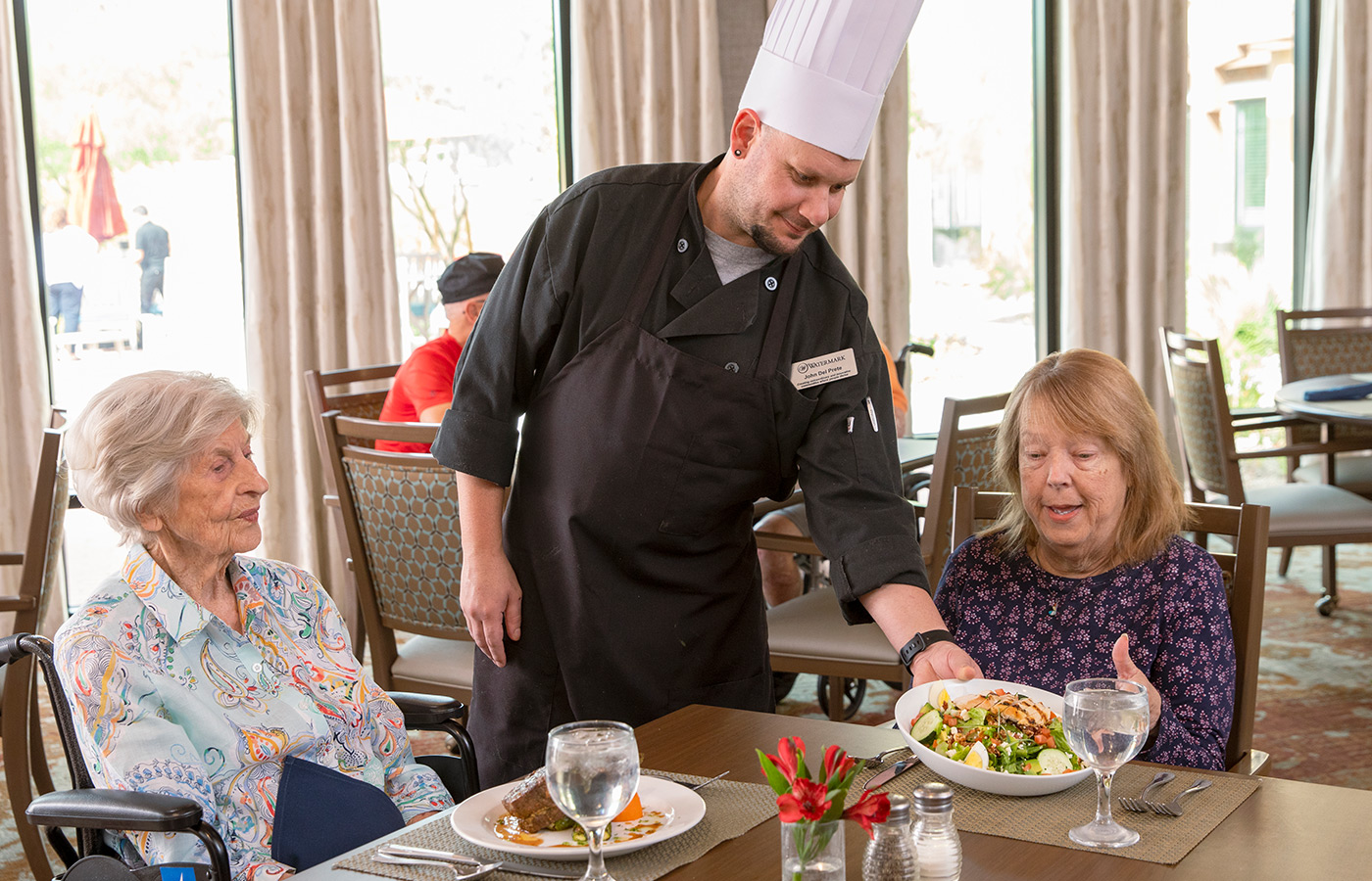 chef placing a plate of food down in front of resident at dining table