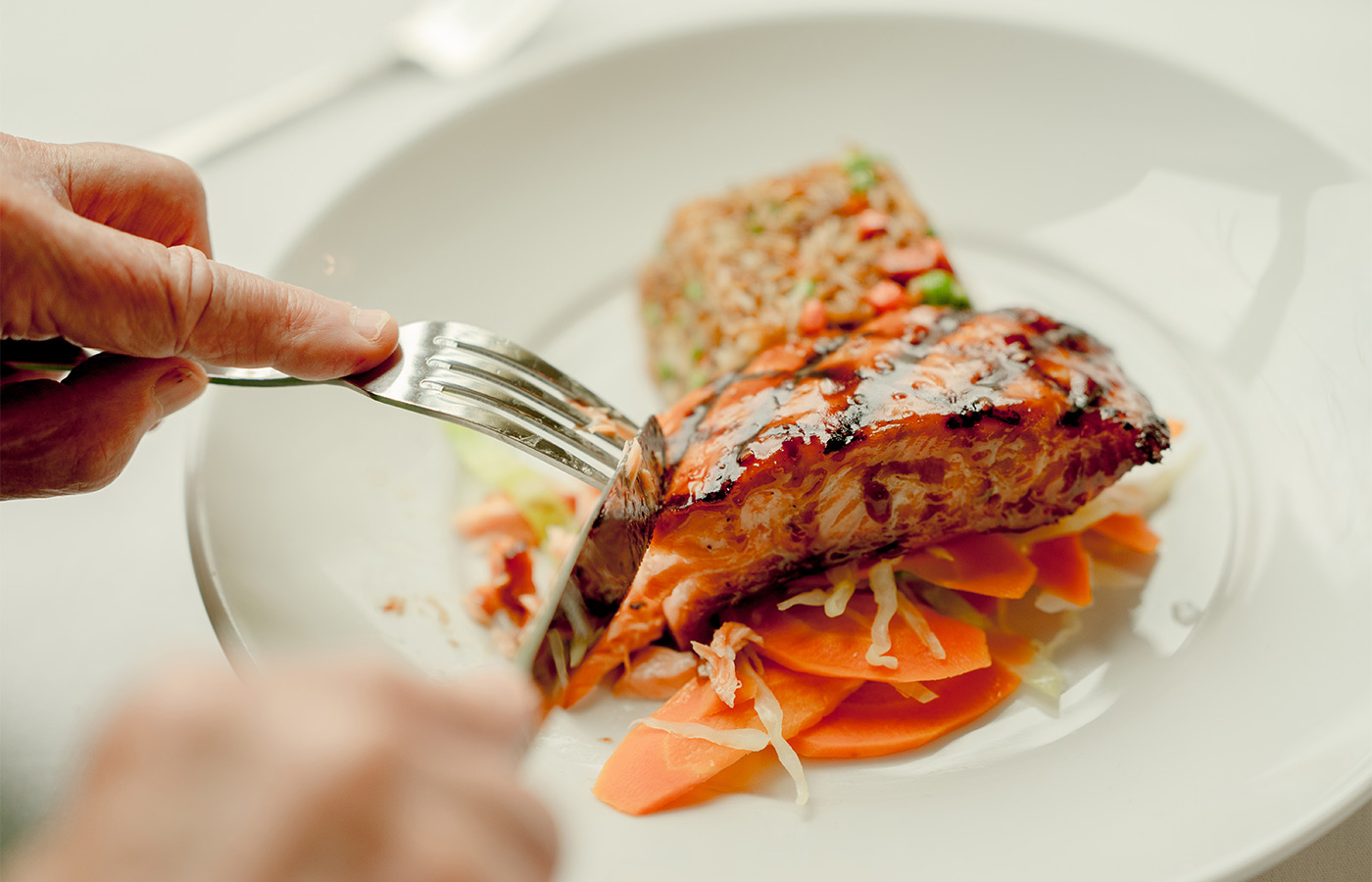 Someone cutting into salmon and rice.