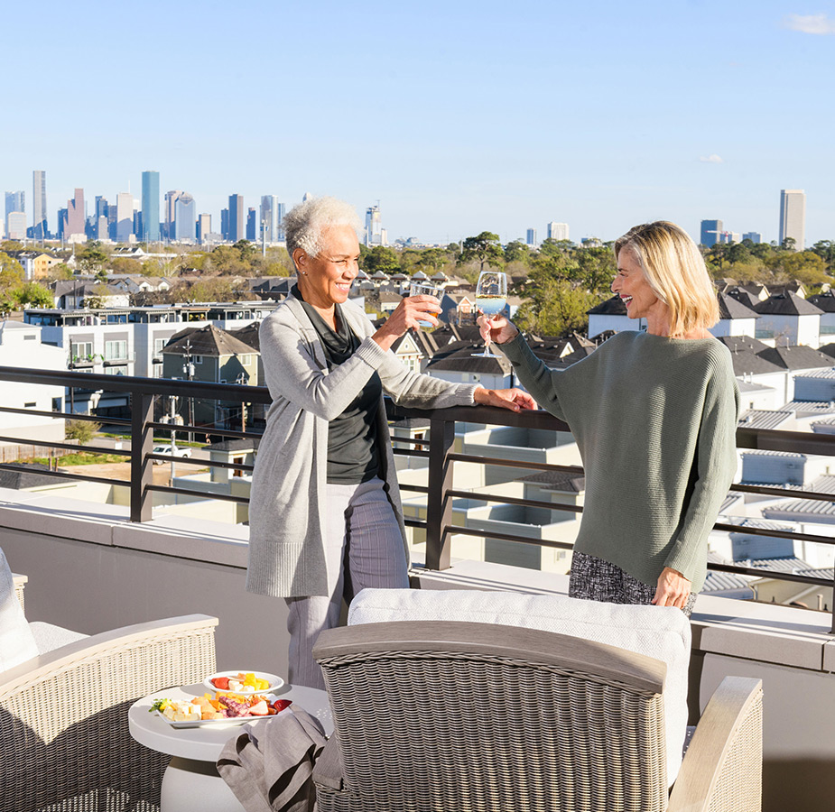 Two residents are standing outside on the rooftop patio enjoying glasses of wine.