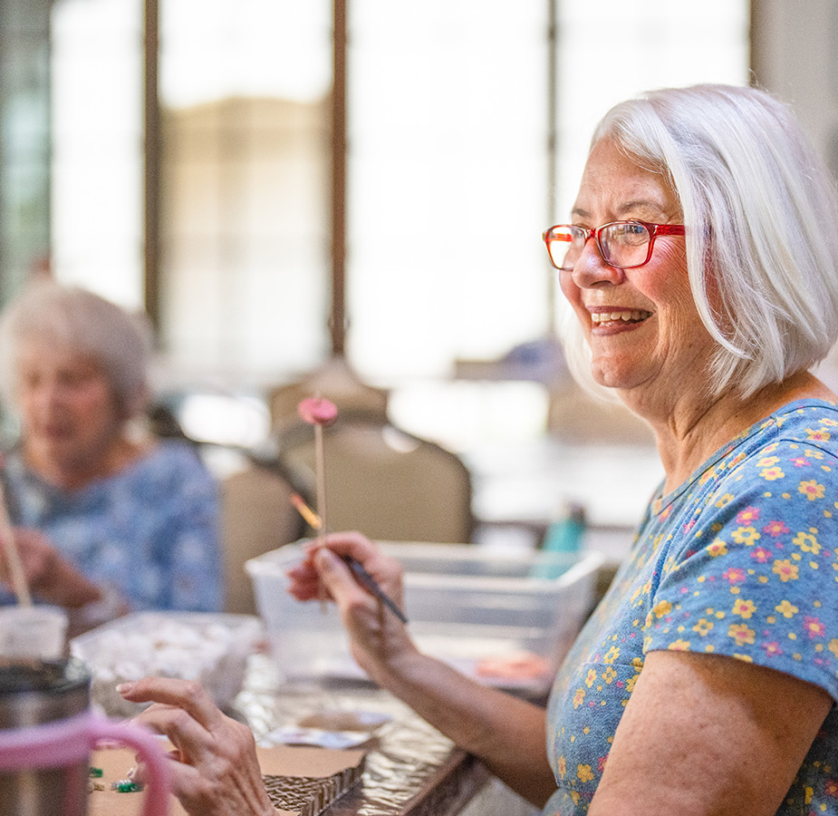 Resident smiles while holding a paintbrush in an art class.