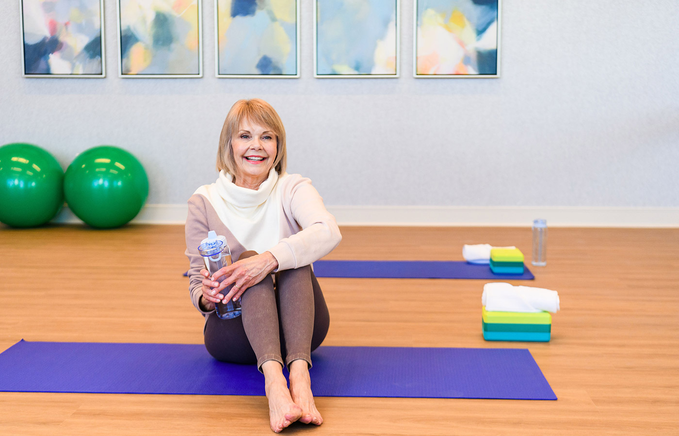 elderly woman smiling and sitting on a yoga mat in fitness room