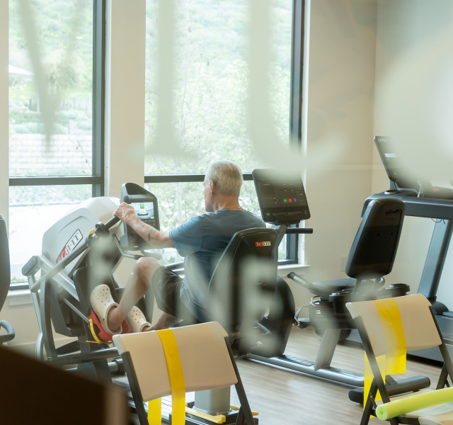 View of fitness center, and a resident using recumbent bike in the background.