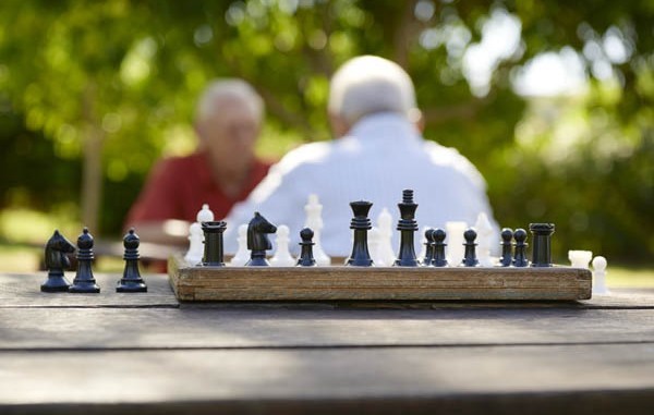 Chess game on table with two residents in the distance playing a game of chess.