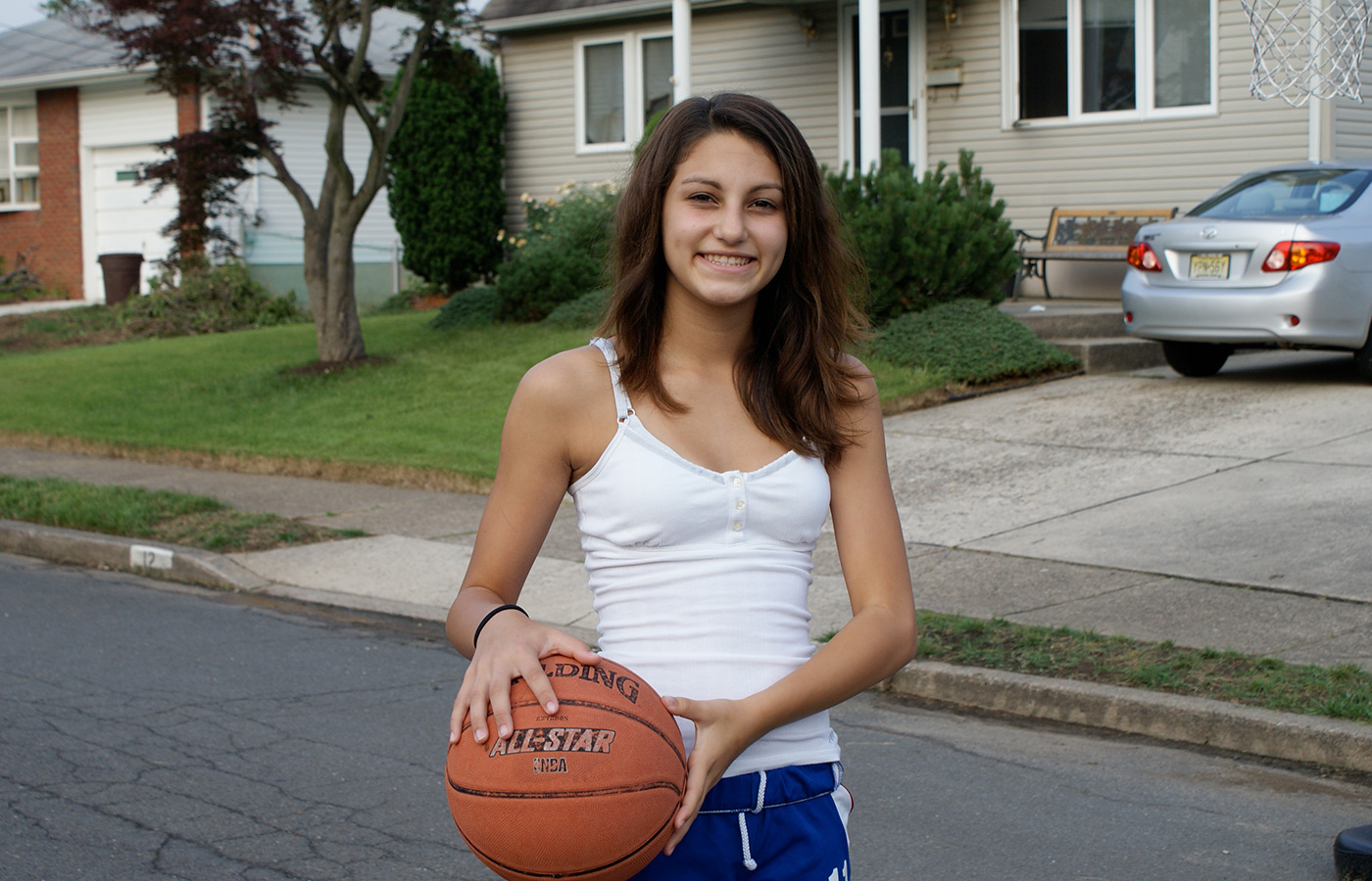 A teen holding a basketball in the street.