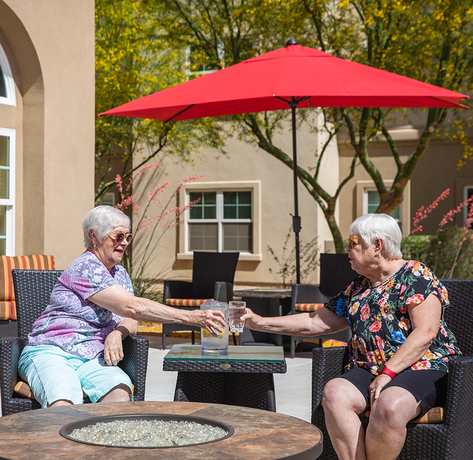 Two residents drink under an umbrella in patio.