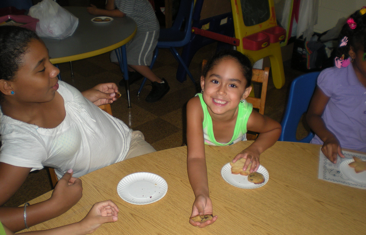 A child reaching across the table with a cookie.