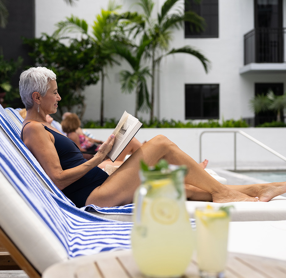 A person lounging, reading a book by the pool.